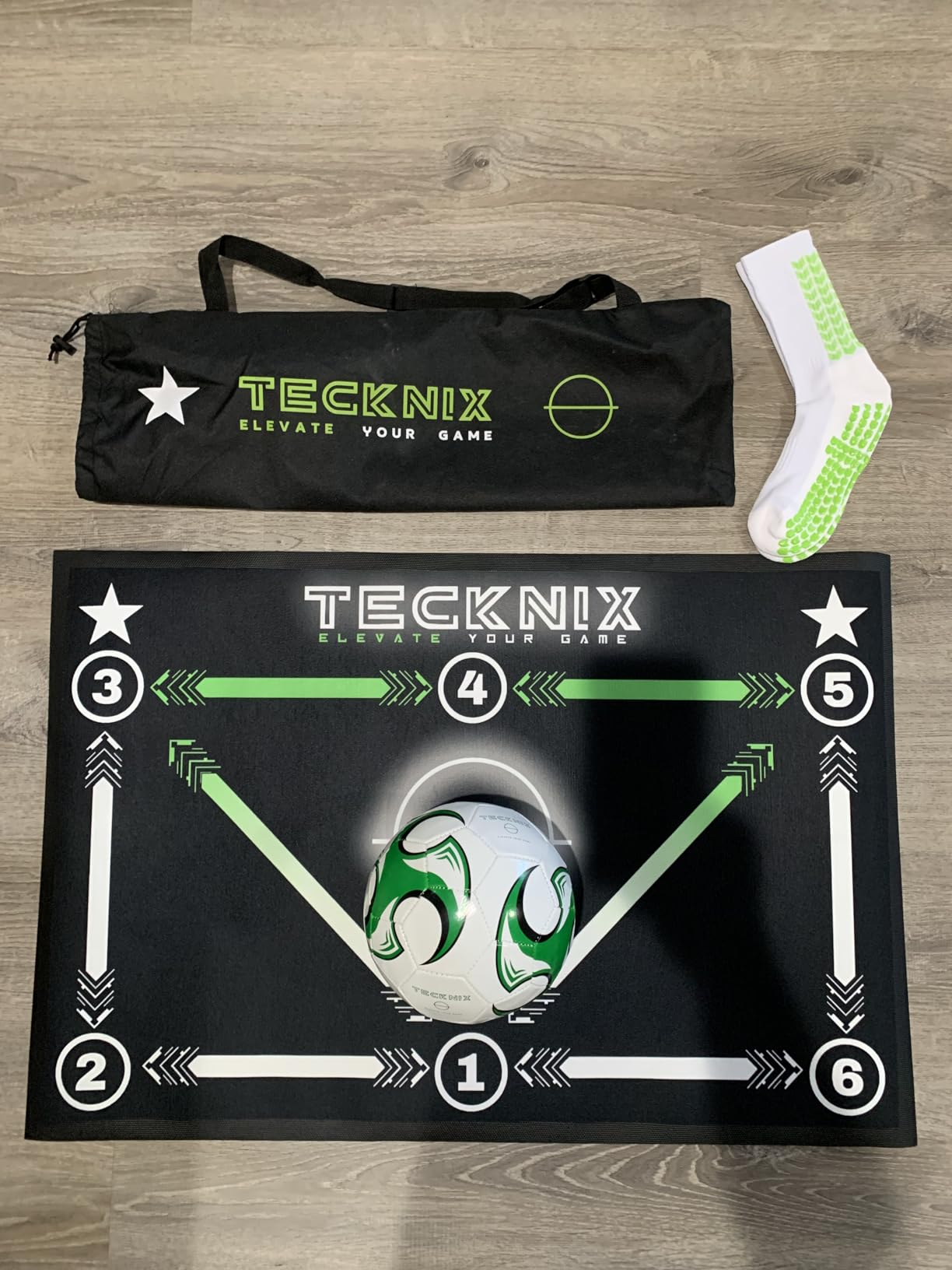 TECKNIX training mat laid flat on a wood floor with a ball, a grip sock and the carry bag