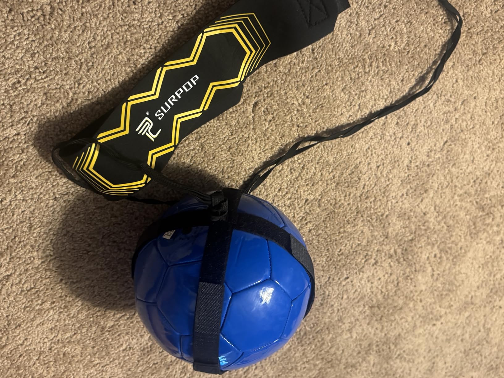 Surpop kick trainer strapped to a blue soccer ball on a carpet