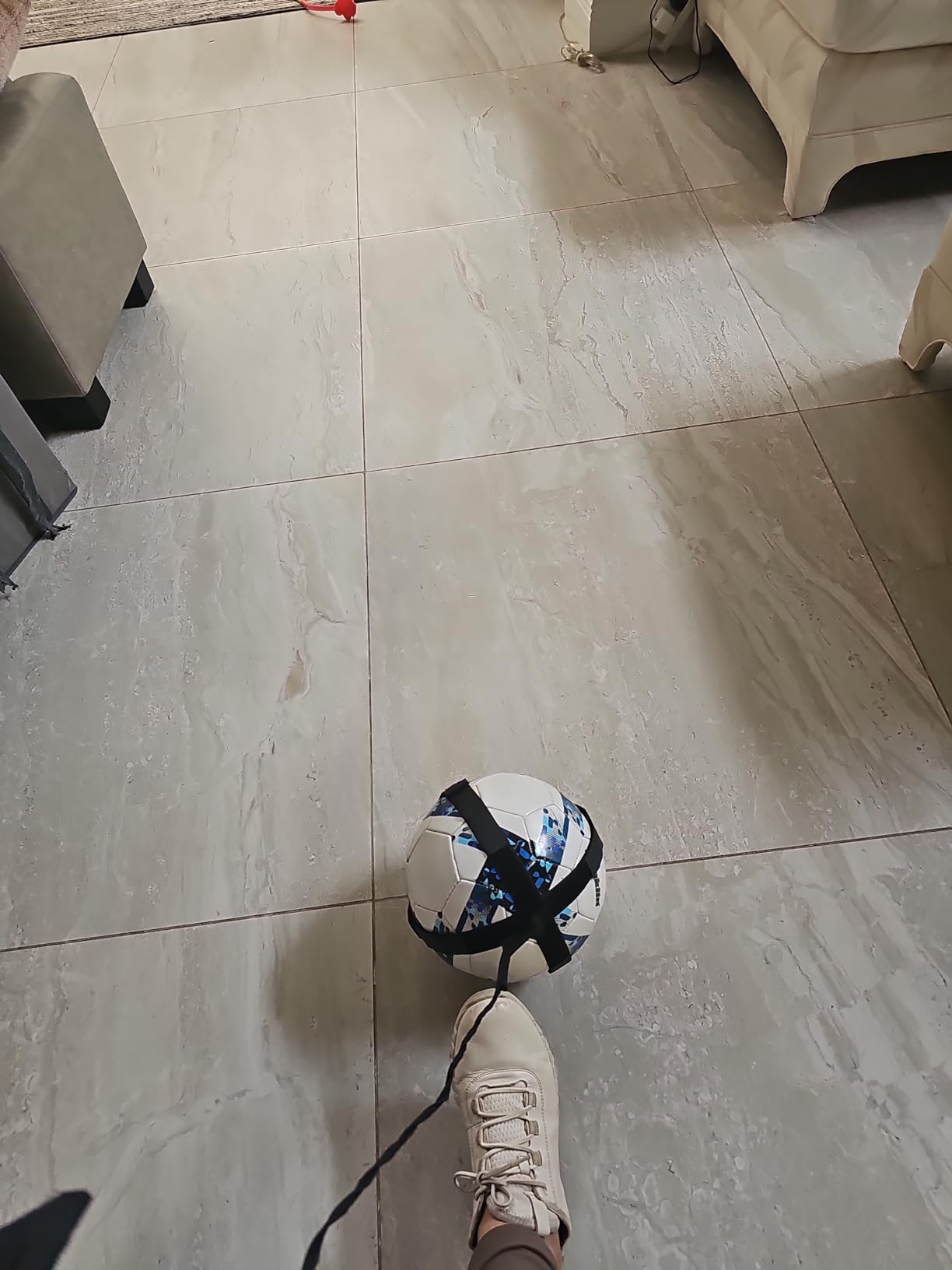 Player dribbling a ball attached to a kick trainer cord across a tiled living room floor
